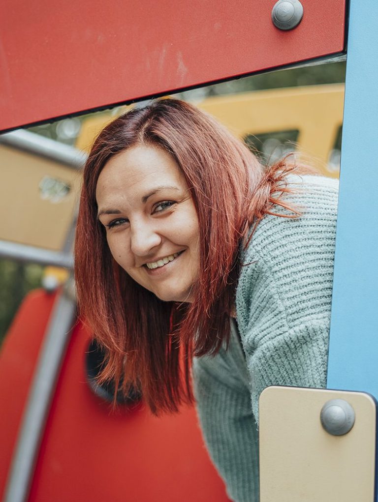 Fotografin in Main Spessart Lächelnde Frau mit roten Haaren beugt sich durch eine Spielzeugstruktur im Freien.