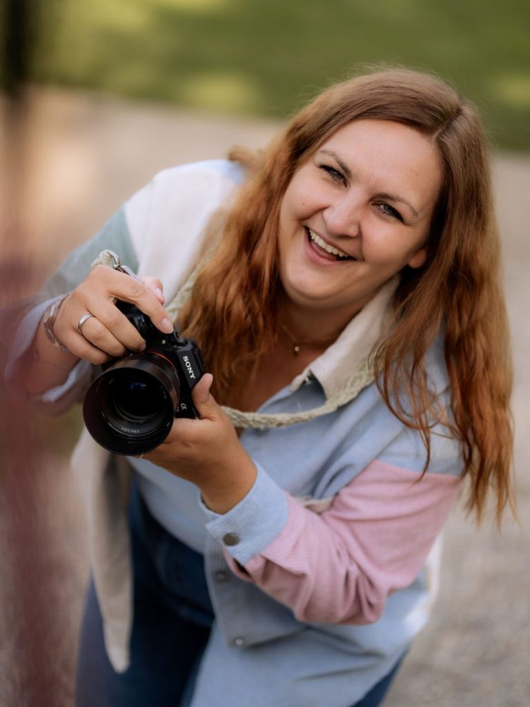 Familienfotografin in Main Spessart & Umgebung Frau mit rotem Haar, die in einem Waldgebiet mit Kamera unterwegs ist.