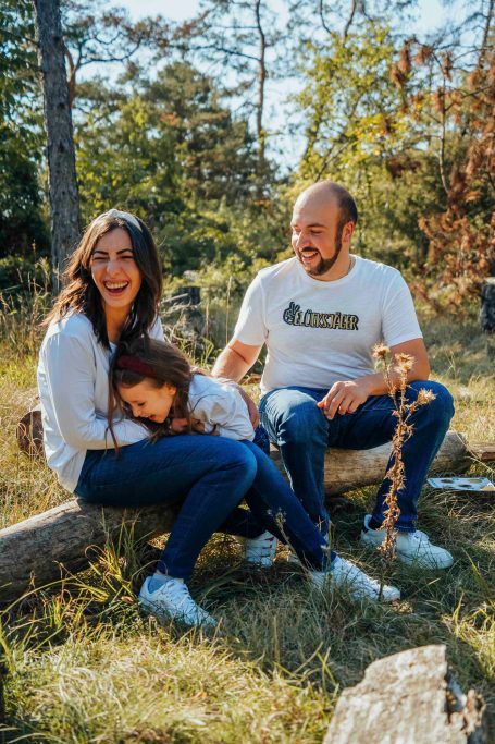 Familie sitzt im Freien auf einem Baumstamm und lacht gemeinsam.