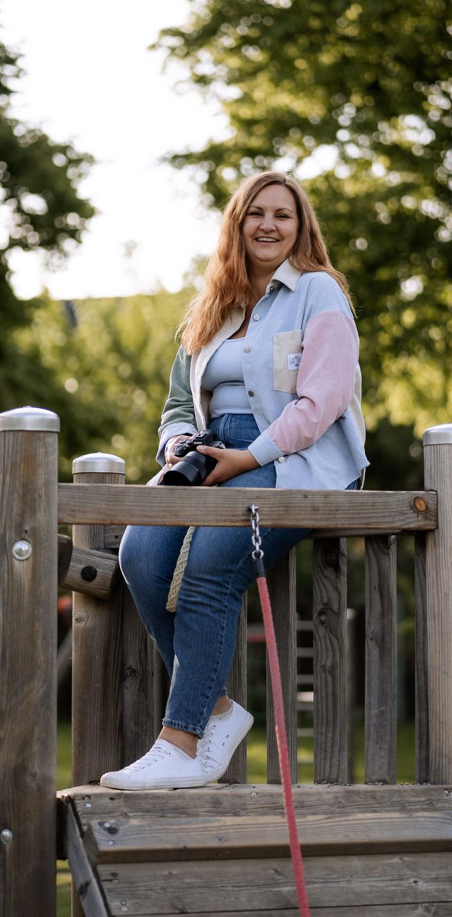 Fotograf Marktheidenfeld Lächelnde Frau mit roten Haaren in einem farbenfrohen Spielplatz-Gerüst.