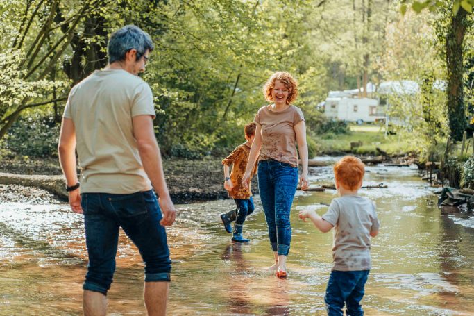 Fotograf Main Spessart und Umgebung Familie beim Spielen in einem kleinen Bach in der Natur, umgeben von Bäumen.