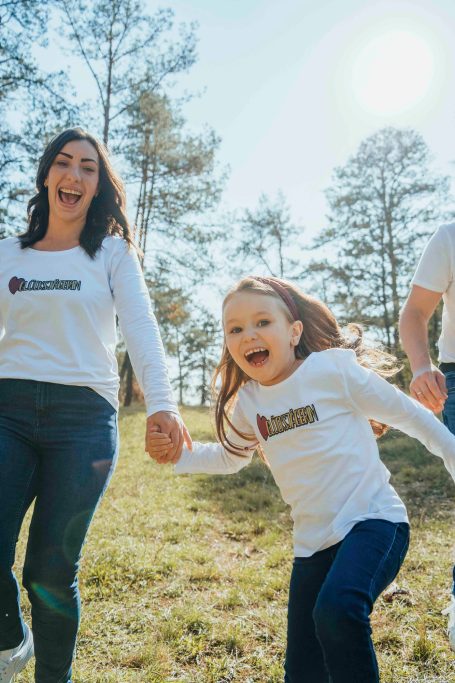 Fotograf Main Spessart und Umgebung Frau und Mädchen halten sich an den Händen und lachen im Freien unter Sonnenlicht.